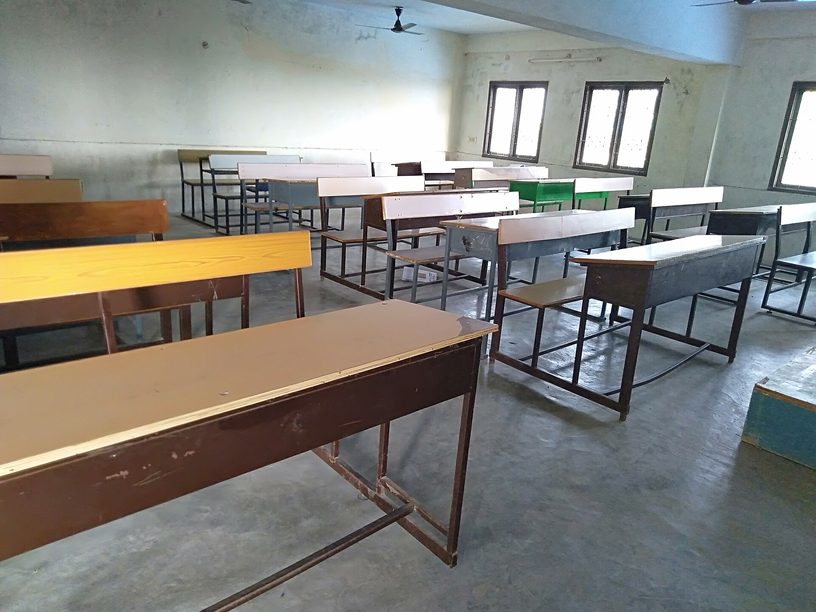 Un aula vacía, con bancos de madera, en una institución educativa.