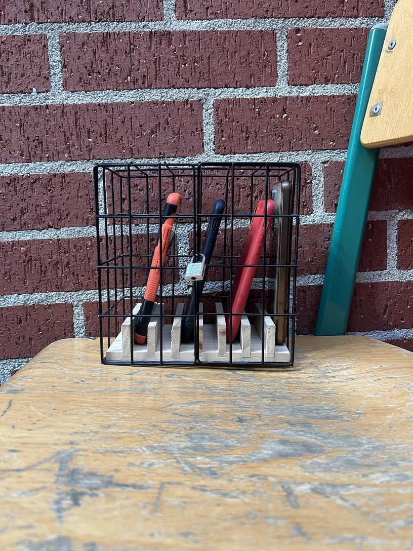 Celulares guardados bajo candado en una caja de alambre, sobre una silla de aula.